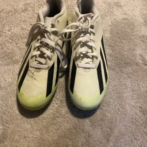 Vita fotbollsskor med svarta ränder - Säljer ett par vita fotbollsskor med svarta ränder och snörning. Skorna har en sportig design med en touch av limegrön färg vid tån. Perfekta för fotbollsplanen!