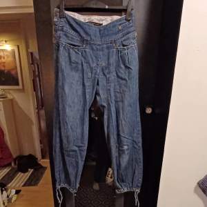 Säljer ett par snygga blå jeans från Nikita Denim. De har en avslappnad passform med resår och snörning vid bensluten för en cool look. Perfekta för vardagsbruk eller en avslappnad utekväll. Märkesloggan är broderad på sidan för en extra touch.