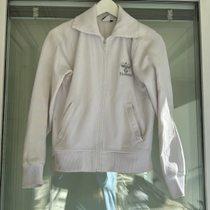 Vit jacka från Hummel - Säljer en snygg vit tröja från Hummel i M. Den har en dragkedja framtill och ribbade muddar vid ärmslut och nederkant. Perfekt för en sportig look eller en avslappnad dag ute. Den är i bra skick (förutom en missfärgning, se bild)