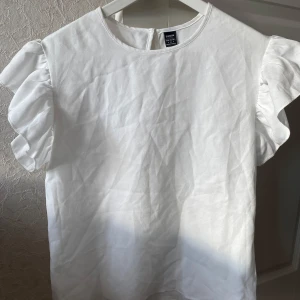 Vit blus med volangärmar - Säljer en söt vit blus i storlek S. Den har korta volangärmar som ger en romantisk touch. Perfekt för både vardag och fest! 💫