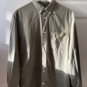 Olivgrön skjorta med knappar - Säljer en stilren olivgrön skjorta med klassisk krage och knappar hela vägen ner. Skjortan har en bröstficka och långa ärmar, perfekt för både vardag och lite mer uppklädda tillfällen. Materialet är 100% linne, och färgen är lätt att matcha.