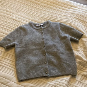 Grå kofta från Zara, pris diskuteras! - Säljer en superfin grå kofta från Zara i storlek S. Den är gjord i ett mjukt material och har korta ärmar. Koftan har snygga knappar framtill och en klassisk rund halsringning. Perfekt för både vardag och lite finare tillfällen. 🩶 används 2 gånger! 