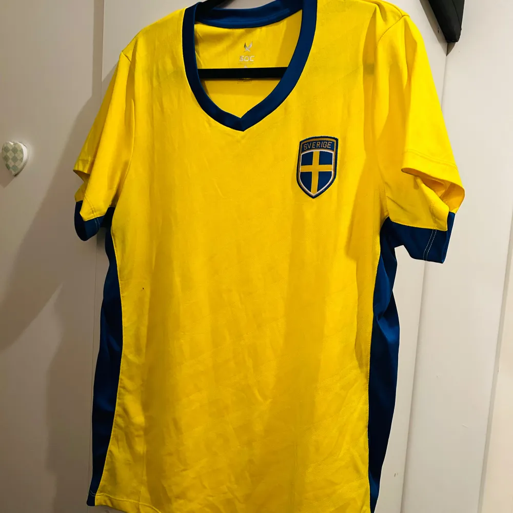 Säljer en gul fotbollströja från SOC med Sveriges emblem på bröstet. Tröjan har korta ärmar och blå detaljer längs sidorna och runt halsen. Perfekt för att heja på Sverige i stil! 🟡🔵. T-shirts.