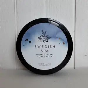 Säljer en burk Swedish Spa Whipped Waves Body Butter från Oriflame. Denna kroppssmör är perfekt för att återfukta och mjukgöra huden. Burken innehåller 200 ml och har en elegant design med en svart lock och en vit/blå etikett med en fin illustration. Perfekt för att skämma bort dig själv eller som en present!