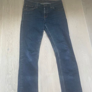 Mörkblå jeans från Nudie Jeans - Säljer ett par mörkblå jeans från Nudie Jeans i storlek W30 L32. Jeansen är i bra skick och har en klassisk femficksdesign med orange sömmar. Perfekta för både vardag och fest!