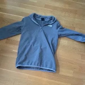 Säljer en grå fleece tröja från The North Face i storlek XS. Tröjan har en halv dragkedja framtill och är supermjuk och varm, perfekt för kyliga dagar. Den är i bra skick och har en enkel, stilren design med The North Face-loggan på bröstet. Perfekt för höst- och vinteraktiviteter!