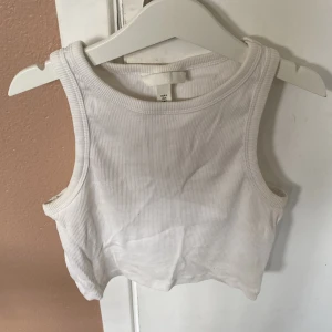 Vit ribbad linnetopp från H&M - Säljer en snygg vit ribbad linnetopp från H&M. Den är ärmlös och croppad, perfekt för sommaren eller träning. Toppen är i storlek S och är i mycket bra skick. Passar både till vardags och fest!