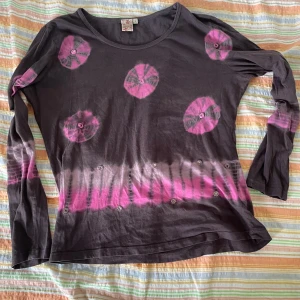 Mörkgrå långärmad tröja med rosa mönster från Anokhi - Säljer en mörkgrå långärmad tröja från Indiska med coola rosa mönster. Tröjan är i bomull och har en avslappnad passform. Perfekt för höst och vår! 🖤💖