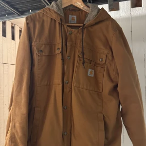 Carhartt jacka brun - Praktiskt taget ny! Använd endast 3 gånger. Köpt för 6 år sedan ny, då för 1700 kr. Storlek M enligt lappen men mer utav en M-L, beroende på hur du vill att den ska sitta. Amerikansk modell nämligen.