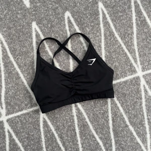 Gymshark sport bh - Svart sport bh från Gymshark. Justerbara band som är korsade i ryggen, V formad framtill. Använd, men i väldigt fint skick.  Storlek XS. Köparen står för frakten 🩷