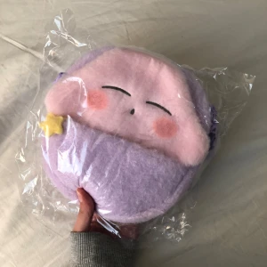 Söt lila axelväska med ansikte - Supergullig Kirby axelväska! Oanvänd! Säljer då den aldrig kommit till användning. Den är mjuk och fluffig. Ca 20 cm hög.