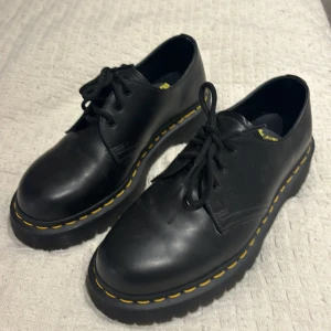 Svarta Dr. Martens skor - Säljer ett par svarta, plattform, låga Dr. Martens skor i storlek 39. Skorna är i skinn och har den klassiska gula sömmen runt sulan. De är i toppskick och har en sula som ger bra grepp. Perfekta för både vardag och fest! Jag accepterar ofta rimliga prisförslag!🤗