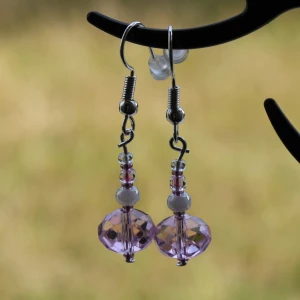 Lila pärlörhängen med kristall - Säljer ett par superfina lila pärlörhängen med kristall. De har en vacker glittrig effekt och är perfekta för att piffa upp vilken outfit som helst. Örhängena är handgjorda och har en unik design med små pärlor och en större kristallpärla längst ner. Passar perfekt till fest eller andra speciella tillfällen.