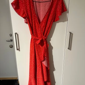 Röd prickig omlottklänning - Från Shein, röd omlottklänning med vita prickar. Klänningen har korta ärmar med volangdetaljer och ett knytband i midjan. 