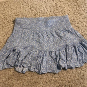 Blå blommig kjol med volang - Säljer en superfin blå kjol med små vita blommor från 157. Kjolen har en elastisk midja och volangdetaljer längst ner som ger den en söt och lekfull look. Perfekt för sommaren! 🦋 