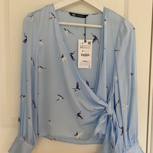 Blå satinblus med pärlor vid ärmarna  - Blå satinblus med pärlor vid ärmarna och fåglar på blusen. Aldrig använd (prislapp kvar). Säljer pga utrensning av garderob. Köpt från zara för 359kr. Storlek XS. 