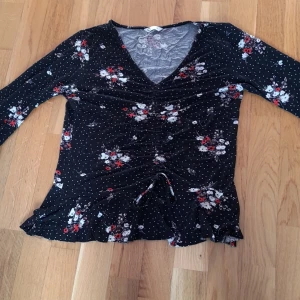 Tröja - En svart blommig tröja som har en fin modell i fram.  Händernas form är kort och fin 