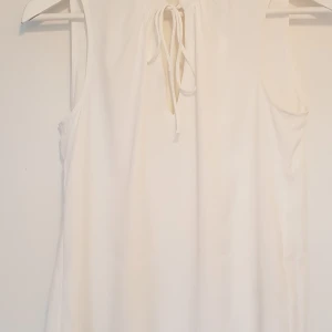 Blus/Linne - Oanvänd blus/linne. Vit chiffongliknande tyg. Knytdetalj. Aldrig använd, nyskick. Pris exkl frakt. Hämtas på lilla Essingen alt mötas upp på Fridhemsplan.