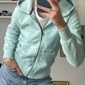 Luvtröja med dragkedja - Ljusblå/ ljust turkos luvtröja från Peak Performance med broderi på ryggen och ena armen. Fint skick!! Ärmarna är tillräckligt långa även för mig som har långa armar🧚