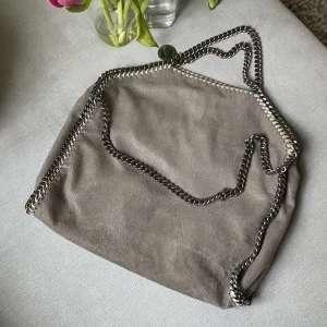 Stella McCartney väska - Stella väska i modellen falabella fold-over tote i färgen light grey. Fint skick, någon slitning på kedjan men inget märks i helhet. Dessutom lite smutsig inuti men inget som märks vid användning. Äkthetsbevis och dustbag finns. Fråga för fler bilder🤗