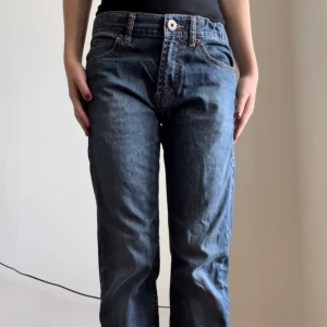 Lågmidjade jeans - mörk blåa lågmidjade jeans med Manchester detaljer. Användt skick och lite slitna längst ner