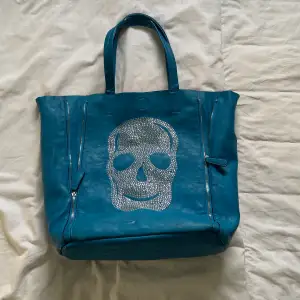 Skitsnygg blå handväska med dödskalle i nitar. Några nitar har ramlat av då den har legat i trångt utrymme pga sällan använd. 