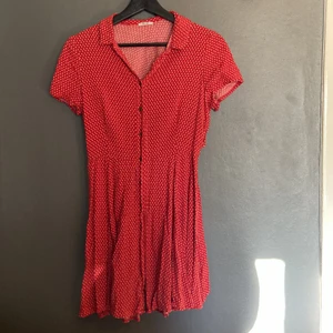Klänning - En röd klänning med vita prickar i härligt material. Knappar hela vägen samt öppet parti i ryggen. 