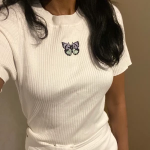 Vit topp med fjäril🦋 - En söt vit kortärmad topp med en fjäril på framsidan🦋 Broderad på tröjan istället för en tryckt bild som i andra fall✨Stickat material. Den är knappt använd och i toppen skick💞