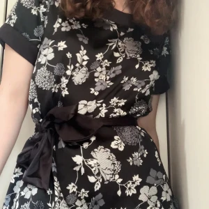 Topp med band - Blommig topp i mjukt, glansigt material med ett band att knyta runt midjan. Den säljs för att den inte används längre då den inte passar, men den har varit en favorit länge och har använts försiktigt. Passar både till vardags och finare tillfällen! 