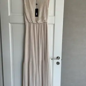 Fantastiskt fin långklänning till sommarens tillställningar. Helt ny! Elegant modell med plisserad kjol i en fin beige färg. Nypris: 400kr. Mitt pris: 200kr. Strl XS. Finns ej i butik!