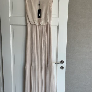 HELT NY Långklänning  - Fantastiskt fin långklänning till sommarens tillställningar. Helt ny! Elegant modell med plisserad kjol i en fin beige färg. Nypris: 400kr. Mitt pris: 200kr. Strl XS. Finns ej i butik!