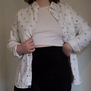 Vit skjorta med mönster - Vit skjorta med mönster av små figurer. Lite missfärgad på insidan av kragen i nacken, men det är inget som syns utåt. Annars i fint skick. 100% bomull. I strl M, true to size. 