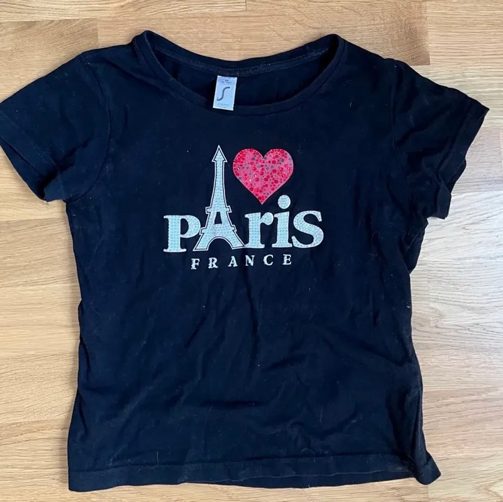 Lånad bild! ”I ❤️ Paris” -baby tee med strass. Köpt på plick och aldrig använd. Tror den är från barnavdelningen men passar mig som har xs/s. Fint skick men lite slitage på hjärtat då några stenar ramlat av. Skriv privat om du undrar något . T-shirts.