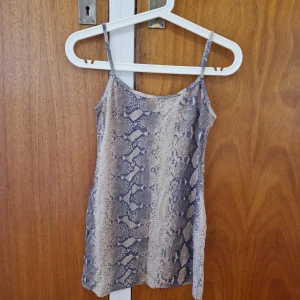 Ormmönstrat figursytt linne - 90-tals stil. Snygg tight passform. Tunnt material. Uppskattar storlek till XS-S. Färgen är beige/gulaktig med inslag av gröna toner.