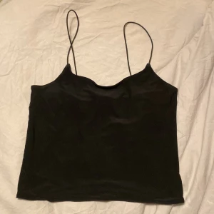 Svart croppad topp - Säljer en svart croppad topp i lite glansigt material. Elastiska axelband. Fint skick. 