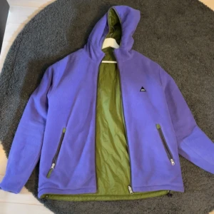 Vändbar jacka  - Döcool lila eller grön jacka. Från Rotation Garments, så går att vända ut och in för en annan färg. Gröna sidan är någorlunda vattentät medans lila är fleeceliknande material. Sitter baggy på mig som är M. 