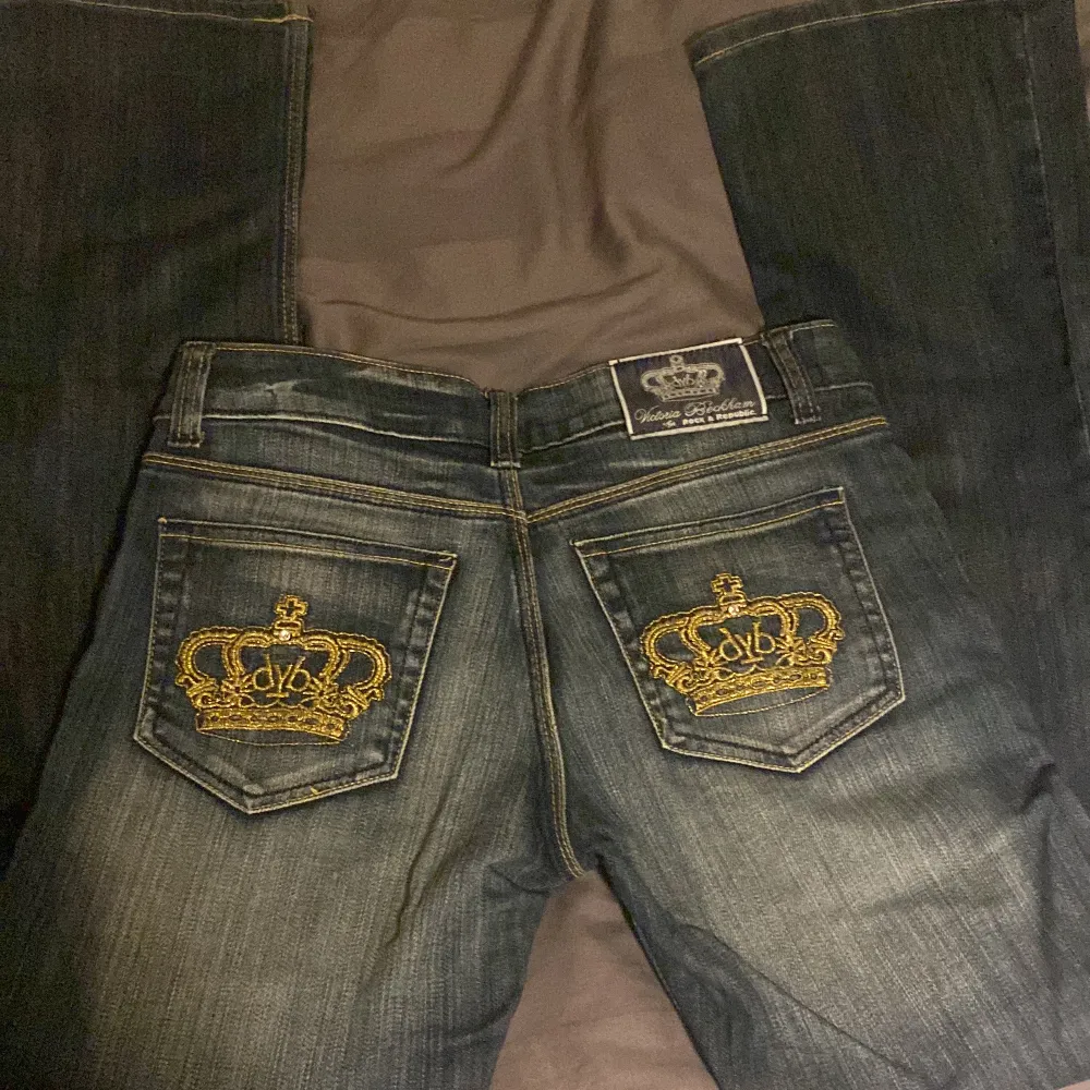 Blåa lågmidjade bootcut Victoria beckhamn jeans,med Guldiga kroner. Bra skick. Storlek 28, midje måtet är 74 cm och innerbenet är 80 cm. 🥰. Jeans & Byxor.