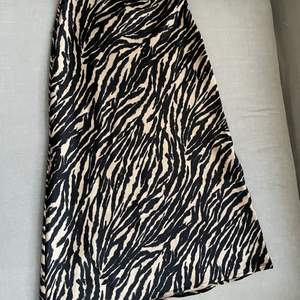 Beige och svart mönstrad knälång kjol i satin liknande material. Använd endast en gång. Mycket fint skick