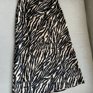 Leopard mönstrad kjol - Beige och svart mönstrad knälång kjol i satin liknande material. Använd endast en gång. Mycket fint skick