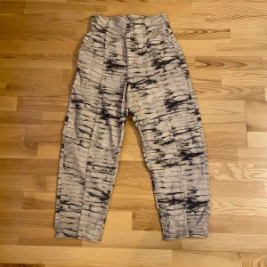 Beiga byxor med grå/svart mönster - H&M byxor med grå/svart camo inspirerat mönster. Byxorna är höga i midjan. Vid modell med avsmalnande ben.