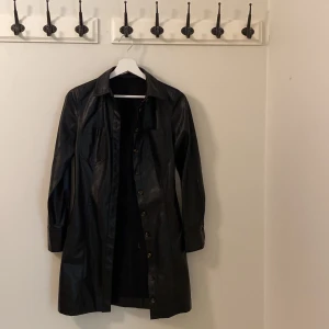 Svart skinn kappa från Mango  - Svart skinn kappa från mango i storlek XS men passar även en S! Kan användas som en skinn klänning också om man knäpper alla knappar!