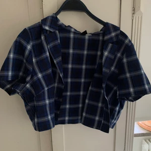 Croppad rutig blå skjorta  - En kort blå och vit rutig tunn skjorta med korta ärmar. Priset är exkl frakt