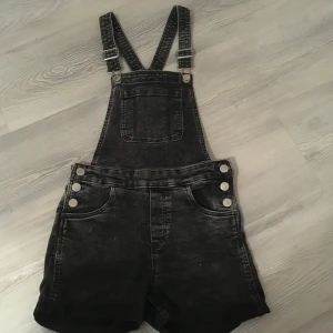 Svarta hängselshorts - Säljer ett par svart/grå hängselshorts i storlek 146 10-11 år. Dom är i väldigt bra skick och har fickor både fram och där bak. Det finns även en ficka vid bröstet. Dom säljs för 70kr +frakt.