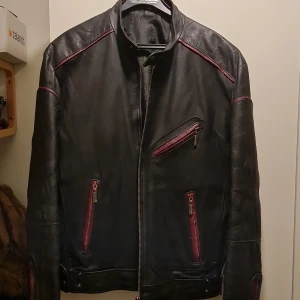 Hollies skinnjacka - Skinnjacka med röda detaljer från hollies. Dragkedjor och knäppknappar för justering av midjan. Väl använd. Lite slitage.