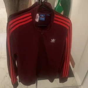 Adidas jacka - Adidasjacka, vinröd färg. Står large i storlek men det än mer medium. 