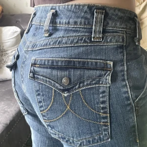 Lågmidjade jeans - Jättesnygga lågmidjade jeans med coola fickor både fram och bak. Jag är 167cm lång. Bra skick, har dock slitningar längst ned vid det som nuddar marken men ser ut som att det ska se ut så. 