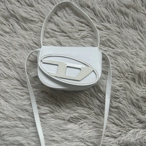 Väska vit - Vit väska i konstläder. Finns både rem för att hålla i handen samt crossbody. Helt ny, aldrig använd. Diesel replika.