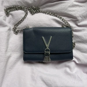 Marinblå Valentinoväska - Jag säljer nu min Mario Valentino väska eftersom jag inte använder den tillräcklig. Inköpt för 799kr på Accent. Kan mötas upp i Uppsala men kan även skicka väskan mot att köpare för står frakt. Den har ett litet veck i vänstra hörnet.