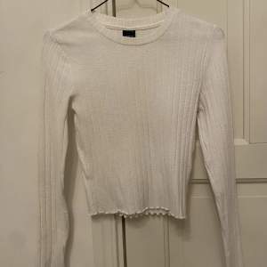 En basic vit långärmad tröja från Gina Tricot i storlek S. Har en slags volang längs ärmarna och nertill. 
