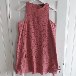 Gammelrosa sommarklänning från Mango - Gammelrosa miniklänning med hög, smal, fyrkantig halsringning i rak model. Bomullstyg med broderade blommor och guldig dragkedja i nacken